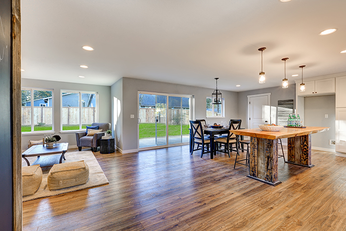 Open floor plan interior with polished hardwood floors showcases an impressive reclaimed wood kitchen island, black dining table set and sliding doors to fenced backyard. Northwest, USA